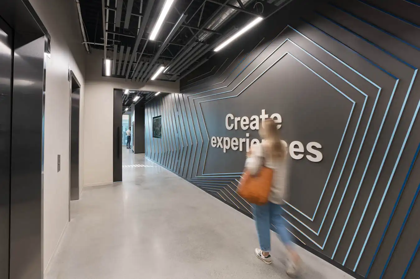 A person walking through a hallway with a wall reading Create Experiences